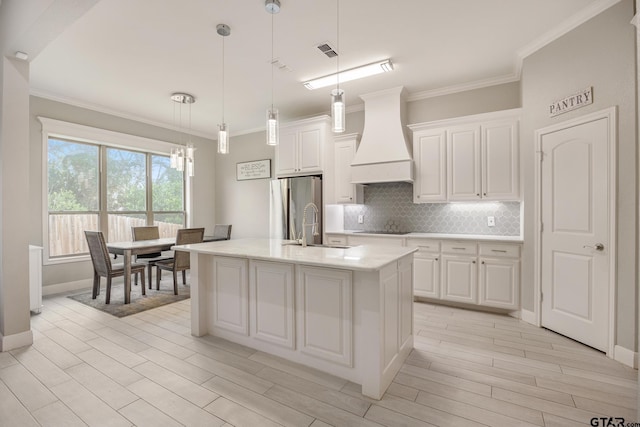 kitchen with stainless steel refrigerator, white cabinetry, a center island with sink, and custom exhaust hood