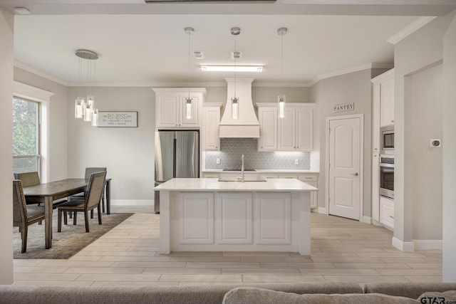 kitchen with custom range hood, decorative light fixtures, appliances with stainless steel finishes, and an island with sink