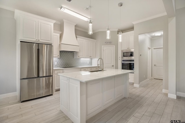 kitchen with white cabinetry, premium range hood, appliances with stainless steel finishes, and an island with sink