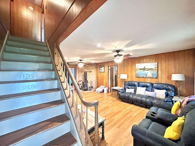 living room featuring wood walls, hardwood / wood-style flooring, ceiling fan, and a wood stove