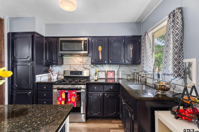 412 W 25th St, Tyler, TX 75702 - kitchen with stainless steel appliances, light wood-style flooring, a textured ceiling, backsplash, and dark stone countertops