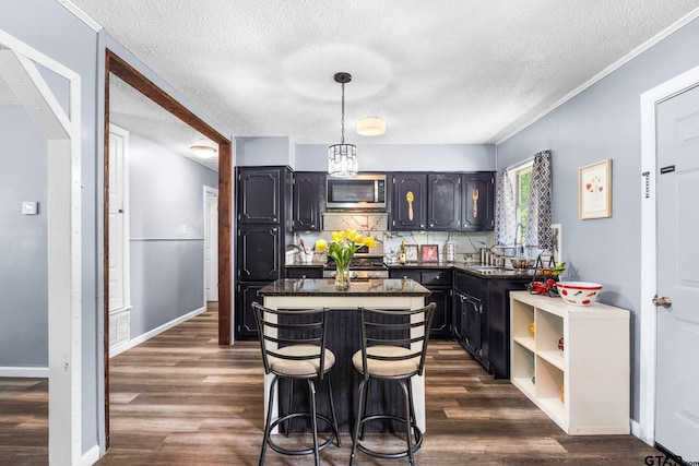 412 W 25th St, Tyler, TX 75702 - kitchen featuring appliances with stainless steel finishes, a textured ceiling, dark countertops, dark wood finished floors, and a kitchen island