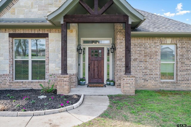 entrance to property featuring brick siding and roof with shingles