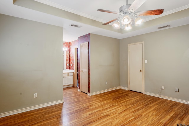 spare room with ceiling fan, a raised ceiling, light wood-type flooring, and ornamental molding