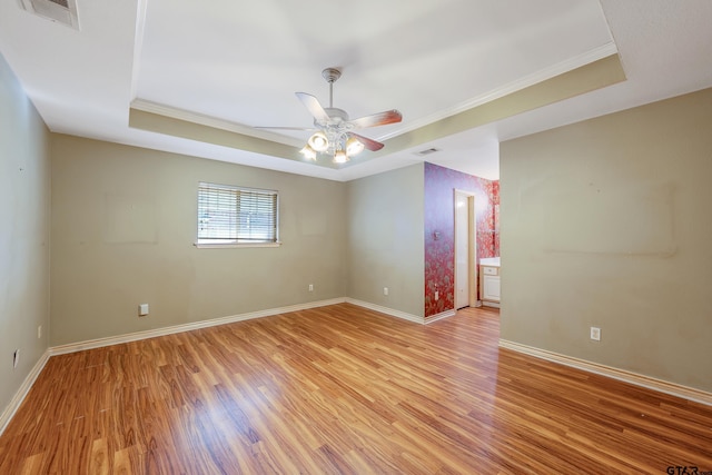 empty room with ceiling fan, a raised ceiling, ornamental molding, and light wood-type flooring