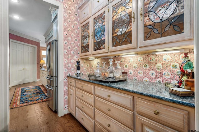 kitchen with dark stone countertops, stainless steel refrigerator, crown molding, and light hardwood / wood-style flooring