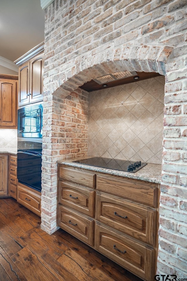 kitchen featuring black appliances, dark wood-type flooring, decorative backsplash, ornamental molding, and light stone counters