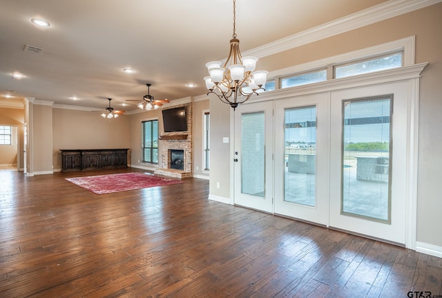 unfurnished living room with dark wood-type flooring, ceiling fan with notable chandelier, ornamental molding, and a brick fireplace