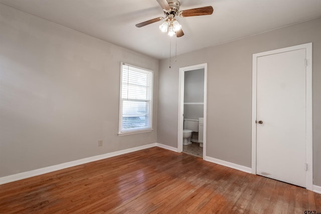 unfurnished bedroom featuring ceiling fan, wood finished floors, connected bathroom, and baseboards