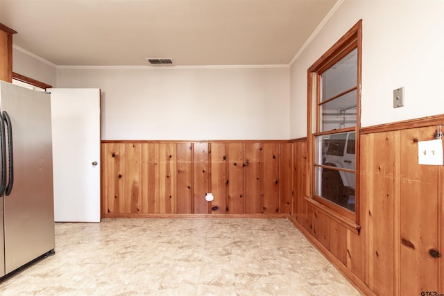 unfurnished room featuring ornamental molding, wainscoting, visible vents, and wood walls