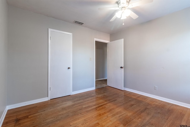 unfurnished bedroom with a ceiling fan, visible vents, baseboards, and wood finished floors