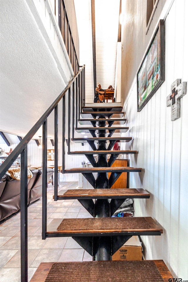 staircase with tile patterned flooring, a textured ceiling, and a towering ceiling