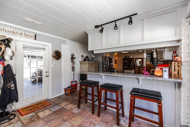 kitchen with white cabinetry, kitchen peninsula, a breakfast bar, stainless steel fridge, and light stone counters