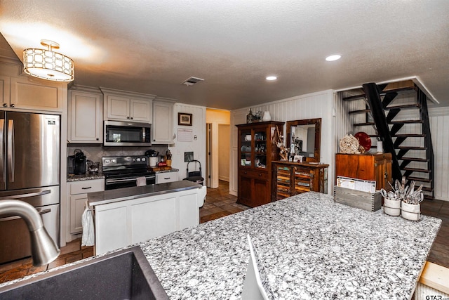 kitchen with appliances with stainless steel finishes, sink, a kitchen island, decorative light fixtures, and light stone countertops