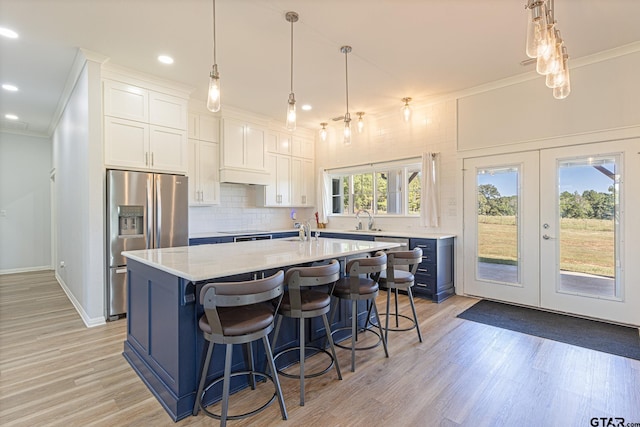 kitchen with white cabinets, sink, light hardwood / wood-style flooring, stainless steel fridge, and an island with sink