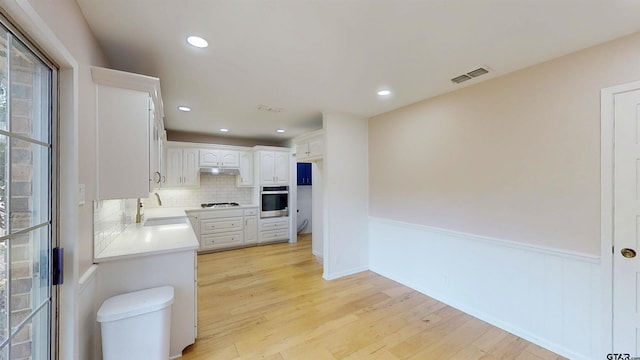 2505 Merry Ln, Tyler, TX 75701 - kitchen featuring stainless steel oven, backsplash, light countertops, white cabinetry, and light wood-type flooring