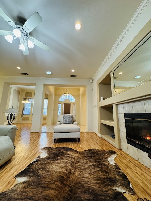 living room featuring ornamental molding, a fireplace, built in features, and light wood-type flooring