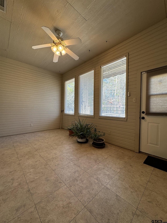 spare room featuring ceiling fan, wood walls, and light tile patterned floors