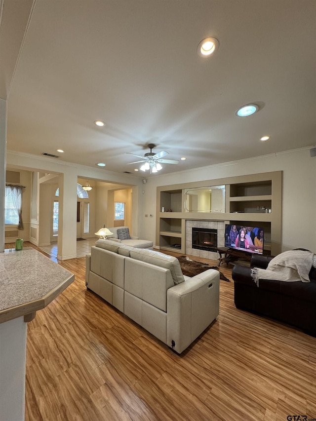 living room with a tile fireplace, ornamental molding, light hardwood / wood-style floors, and built in shelves