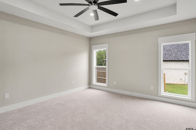 carpeted empty room featuring ceiling fan and a raised ceiling