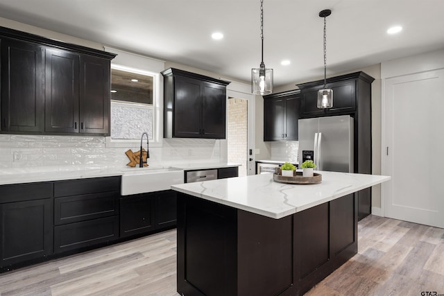 kitchen featuring a center island, decorative light fixtures, stainless steel appliances, sink, and light hardwood / wood-style flooring