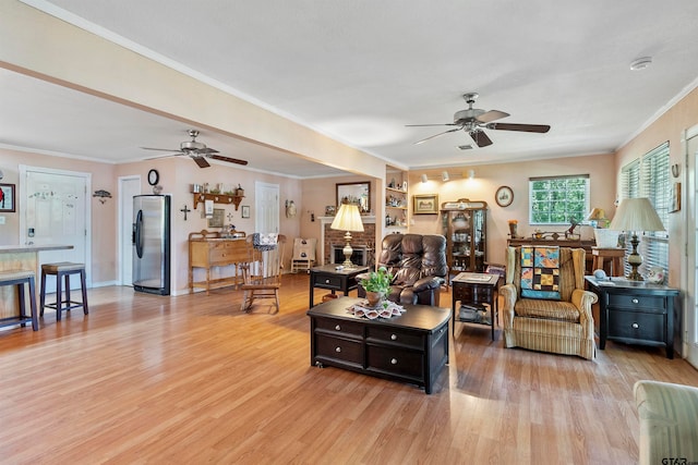 living room with light wood-type flooring, ceiling fan, ornamental molding, and a fireplace