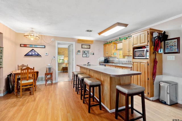 kitchen with light wood-type flooring, a notable chandelier, a breakfast bar area, and light brown cabinetry