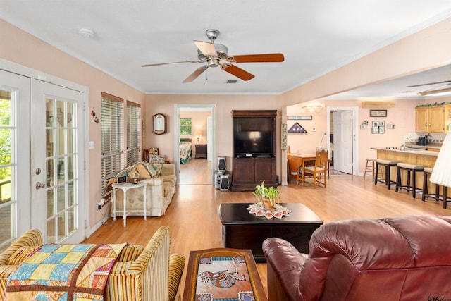 living room featuring ceiling fan, crown molding, light wood-type flooring, and french doors