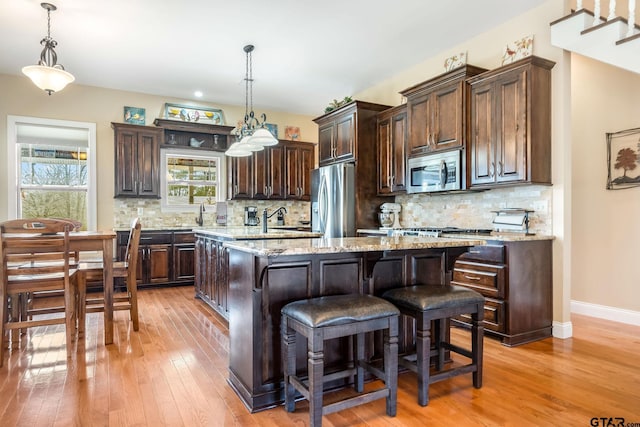 kitchen with dark brown cabinetry, hanging light fixtures, an island with sink, and appliances with stainless steel finishes