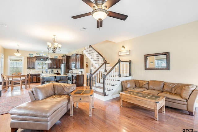 living room with ceiling fan with notable chandelier and light wood-type flooring