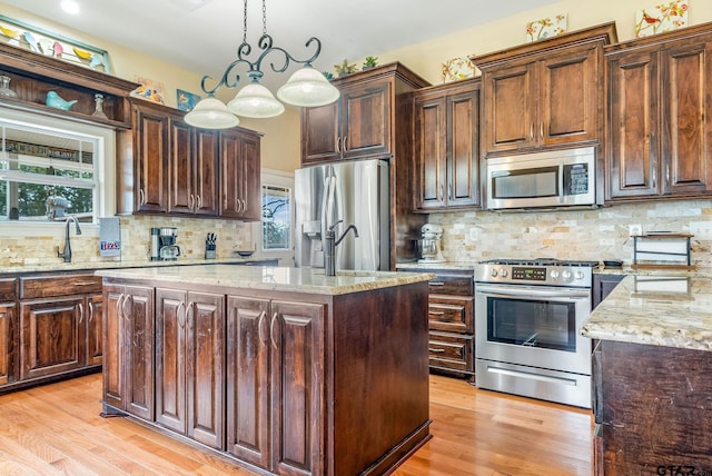 kitchen featuring a center island, appliances with stainless steel finishes, pendant lighting, light stone countertops, and light hardwood / wood-style floors