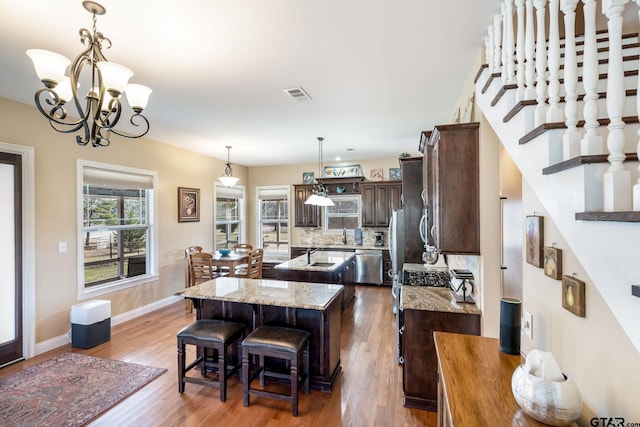 kitchen with dark brown cabinets, a kitchen island, light stone counters, tasteful backsplash, and a kitchen bar