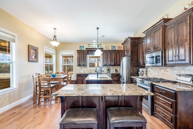 kitchen featuring pendant lighting, dark brown cabinetry, appliances with stainless steel finishes, and a center island with sink