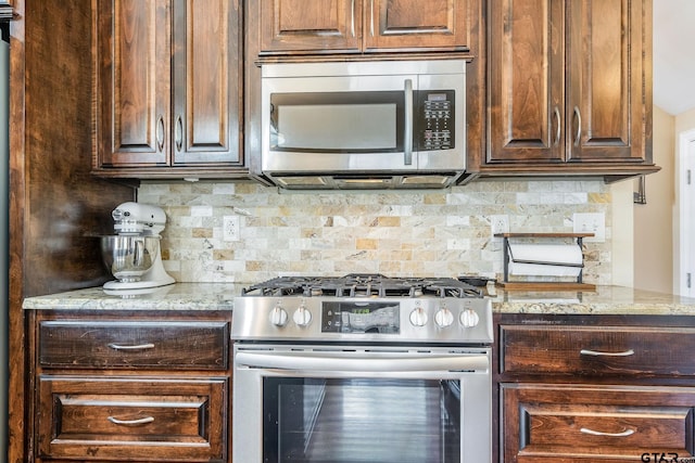 kitchen featuring light stone counters, backsplash, dark brown cabinets, and stainless steel appliances