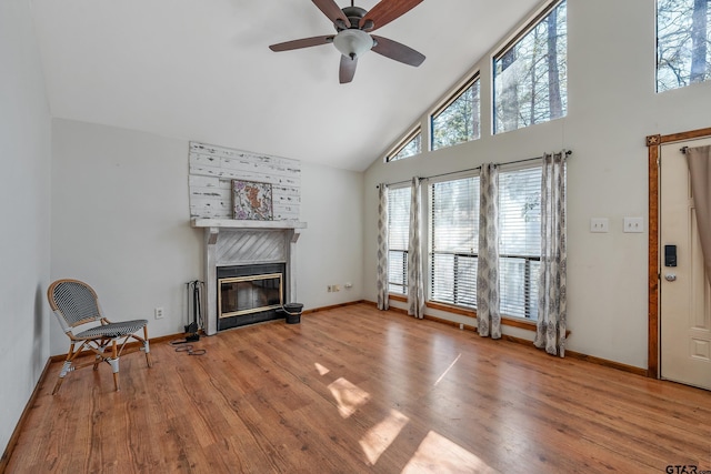 living room featuring high vaulted ceiling, wood finished floors, a ceiling fan, baseboards, and a tiled fireplace