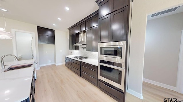 19346 Aida Dr, Flint, TX 75762 - kitchen featuring appliances with stainless steel finishes, wall chimney range hood, light wood finished floors, dark brown cabinetry, and recessed lighting