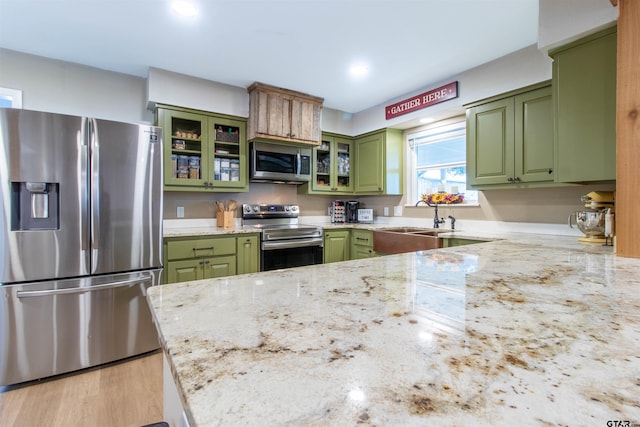 kitchen featuring light stone countertops, stainless steel appliances, green cabinetry, and sink