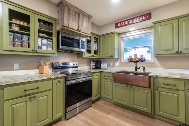 kitchen with appliances with stainless steel finishes, light stone counters, sink, light hardwood / wood-style flooring, and green cabinetry