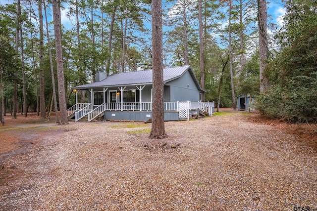 view of front of property with an outbuilding, a chimney, covered porch, a storage shed, and metal roof