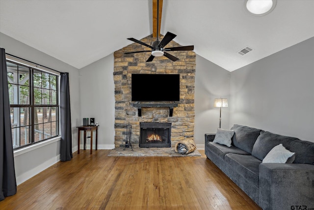 living area featuring visible vents, baseboards, lofted ceiling with beams, wood-type flooring, and a stone fireplace