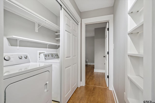 clothes washing area featuring baseboards, laundry area, light wood-style flooring, and washer and dryer