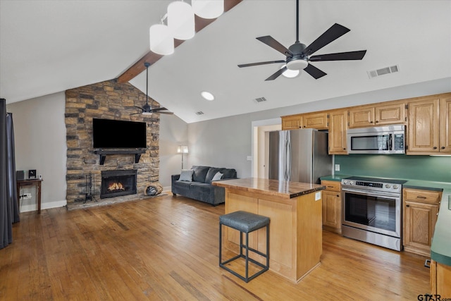 kitchen with stainless steel appliances, a fireplace, a kitchen island, visible vents, and open floor plan