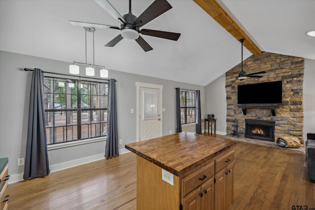 kitchen with lofted ceiling with beams, ceiling fan, a stone fireplace, butcher block countertops, and light wood-type flooring