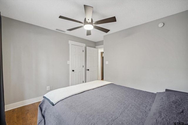 bedroom featuring baseboards, dark wood finished floors, visible vents, and a ceiling fan