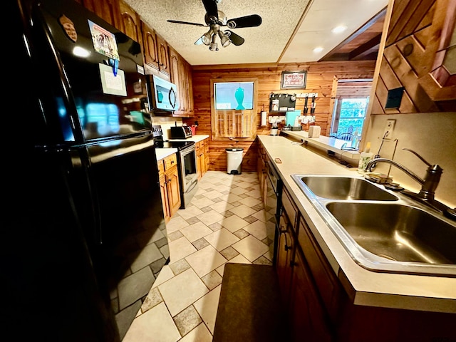 kitchen with ceiling fan, sink, stainless steel appliances, a textured ceiling, and wooden walls