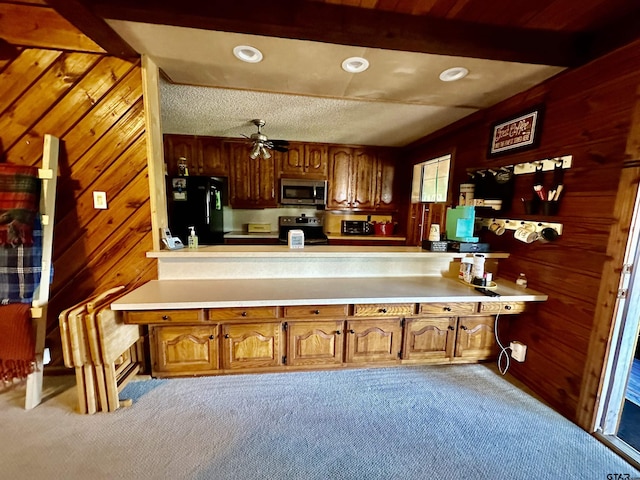 kitchen featuring beam ceiling, ceiling fan, wood walls, light colored carpet, and black appliances