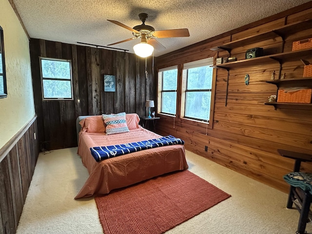 carpeted bedroom with a textured ceiling, ceiling fan, and wooden walls