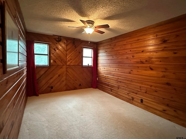 carpeted spare room with a textured ceiling, ceiling fan, and wooden walls