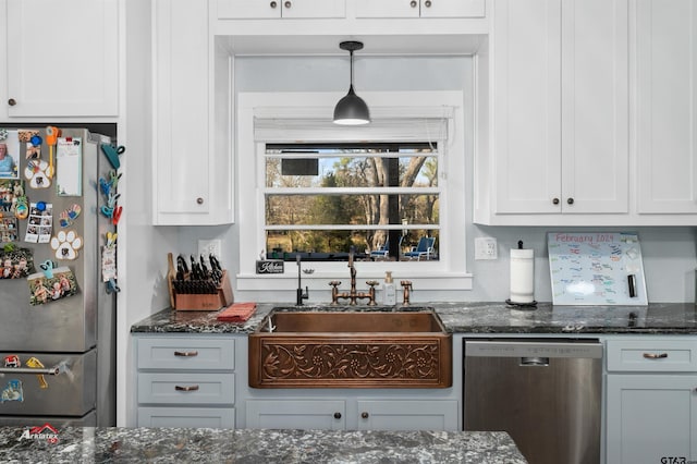 kitchen featuring dark stone countertops, stainless steel appliances, a sink, and white cabinetry