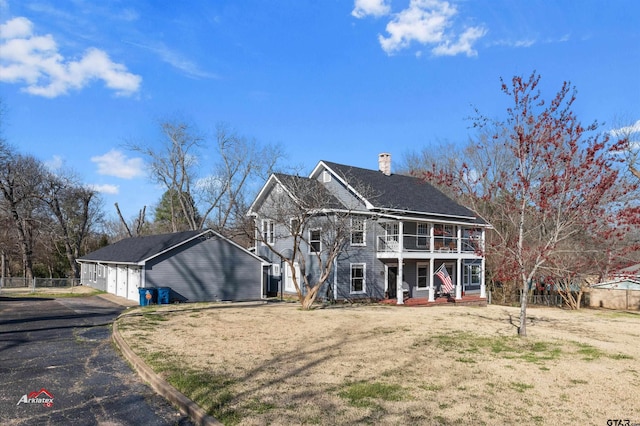 view of front facade featuring fence, a front yard, covered porch, a chimney, and an outbuilding